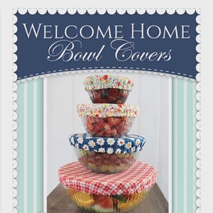 May include: A stack of four glass bowls filled with fruit, each topped with a fabric bowl cover. The top cover features a fruit print, the second has a fruit pattern, the third is blue with white flowers, and the bottom is red and white gingham.