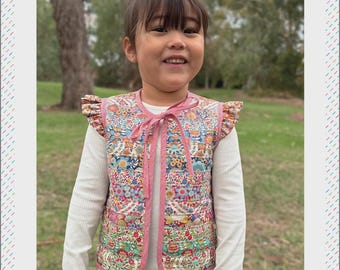 May include: A child wearing a reversible patchwork vest with a floral pattern. The vest has pink trim and a bow closure. The text "HARMONY VEST" and "Melly and Me" are visible.