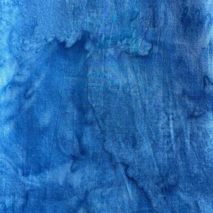 May include: Close-up of a blue fabric with a tie-dye pattern. The fabric has a textured appearance with darker blue areas creating a mottled effect. The overall color is a vibrant, medium blue.