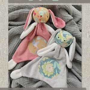 May include: Two plush bunny loveys in pink and gray, with floral and bird-themed patches. The bunny heads feature patterned fabric, and the ears are pink and white. The text "Molly & Me" and "Lovey Love" are visible.