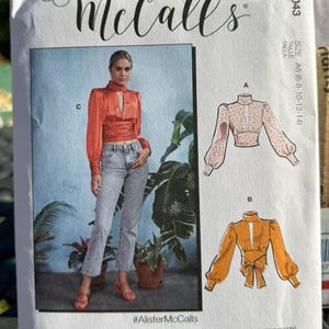 May include: McCall's sewing pattern M8043 featuring a woman wearing a red blouse and jeans. The pattern includes multiple view options. The size is A5 (6-8-10-12-14).
