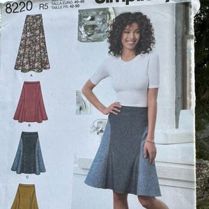 May include: Simplicity sewing pattern 8220 for a skirt in sizes U.S. 14-22. The envelope displays a white short-sleeved top and a knee-length skirt with dark gray and light blue panels. Four skirt variations are illustrated on the left side.