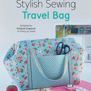 May include: A light blue travel bag with a floral pattern, featuring two handles and a zipper closure. The text reads: Stylish Sewing Travel Bag, Hardware Included, Designed by Kristyne Czepuryk of Pretty by Hand. Sewing tools are visible nearby.