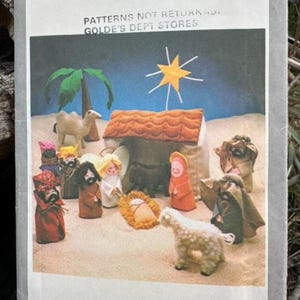 May include: A Simplicity 8776 sewing pattern envelope featuring a nativity scene illustration. The image displays a stable, a yellow star, a camel, a sheep, and several figures in colorful robes on a sandy surface. Text includes Simplicity 8776.