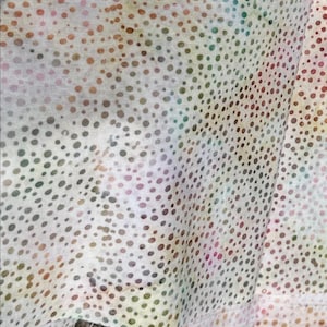 May include: White fabric with a colorful polka dot pattern. The dots are various shades of brown, green, and pink. The fabric is sheer and has a slight sheen.