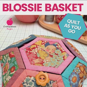 May include: A Blossie Basket quilt with a floral design and a button closure. The quilt features a woman's face in the center and the text "Quilt As You Go". The quilt is made of various fabrics in shades of pink, blue, and green.