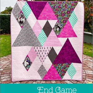 May include: A modern quilt with a geometric design featuring triangles and diamonds in shades of pink, purple, gray, and teal. The quilt includes framed portraits and the text "End Game".