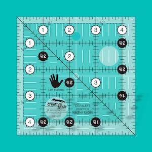 May include: A clear, square quilting ruler with a teal grid pattern and black and white markings. The ruler features measurements in inches, with numbers and diagonal lines for precise cutting. The text "Left-Handed" and "creative grids" are visible.