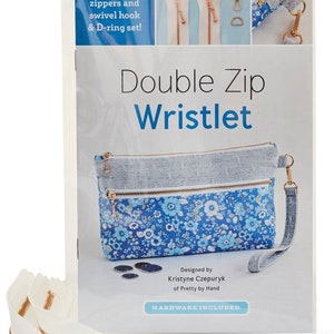 May include: A Double Zip Wristlet sewing kit. The kit includes zippers, a swivel hook, and a D-ring set. The wristlet design features a blue floral pattern and a gray fabric. The text on the package reads "Double Zip Wristlet".