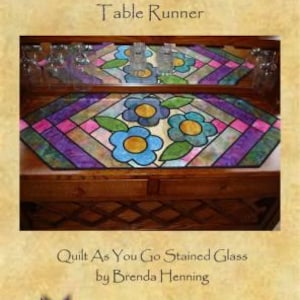 May include: A stained glass table runner with a floral design featuring blue and yellow flowers, green leaves, and a geometric border. The text "Forget-Me-Not Table Runner" is displayed above the runner.
