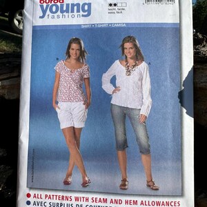 May include: A Burda Young Fashion sewing pattern envelope, number 7824, featuring two shirt designs. One view shows a short-sleeved floral print top with white shorts, and the other shows a long-sleeved white textured top with blue denim capri pants.