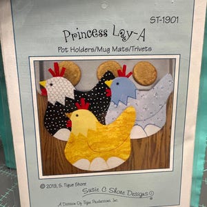 May include: Princess Lay-A pot holders, mug mats, and trivets. The design features three colorful chicken shapes in black and white polka dots, yellow, and blue. The text "Princess Lay-A" and "Susie C Shore Designs" are visible.