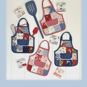 May include: Three quilted apron-shaped hot pads featuring patchwork fabric in red, white, and blue patterns with lace-trimmed pockets and D-rings. The text reads Apron Hot Pads, JMD-229, and Stitch a set of adorable Apron Hot Pads, 9 inches high by 8 inches wide.