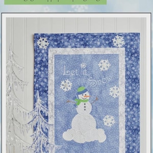 May include: A wall hanging with a blue and white snowflake pattern and a snowman design. The text "Let It Snow, Man!" is at the top. The wall hanging is made with appliqué and quilting designs.