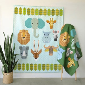 May include: A light blue quilt featuring geometric animal designs, including an elephant, giraffe, lion, and zebra. A matching green blanket with similar animal patterns is draped over a wooden stand. The quilt and blanket are part of a nursery or children's room theme.