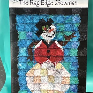 May include: A quilt pattern titled "Frosty The Rag Edge Snowman." The image features a snowman design with a black top hat, red vest, and a patchwork body. The background is a textured blue and green pattern. The text "Saginaw St QUILTS" is at the bottom.