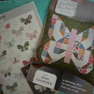 May include: Two Lella Boutique pattern books. One features butterfly designs, the other shows a butterfly-shaped pillow or mini quilt. The pillow is made of patchwork squares in various colors. The text "MINI CHARMED" is visible.