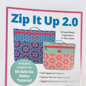 May include: Two rectangular fabric organizers labeled Zip It Up 2.0. The larger bag features a blue and pink geometric pattern, while the smaller bag has a green and yellow geometric pattern. Both include a top handle and a pink zippered closure.