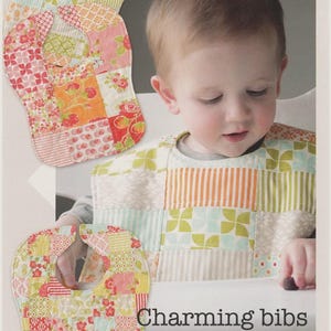May include: A sewing pattern titled Thimble Blossoms by Camille Roskelley, number 153, featuring instructions for Charming bibs, big bibs for little ones. The cover displays two patchwork bibs made from various floral and striped fabric squares.