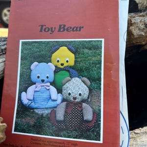 May include: A red paper sewing pattern envelope titled A Patchwork Pattern and Instructions by Yours Truly Toy Bear. The cover features three fabric teddy bears in blue gingham, yellow, and floral patterns, with text stating finished size 17 inches.