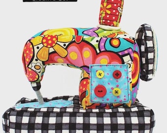 May include: A colorful, fabric sewing machine pin cushion with a black and white checkered base. The machine features a vibrant floral design, a red and yellow spool, and decorative buttons. The text "Sewing Machine Pin Cushion Sewing Pattern" is visible.