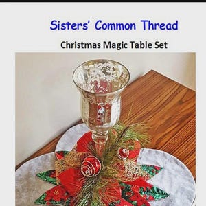 May include: A Christmas Magic Table Set with a clear glass candle holder, red and gold ornaments, and a poinsettia-shaped table runner. The text "Sisters' Common Thread" and "Christmas Magic Table Set" are visible.