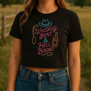Puede incluir: Top corto negro con el texto de ne&oacute;n "Whiskey Bent & Hell Bound" con un sombrero de vaquero y un gr&aacute;fico de botella de whisky. La camiseta se combina con vaqueros azules. El dise&ntilde;o es en rosa, amarillo y azul.