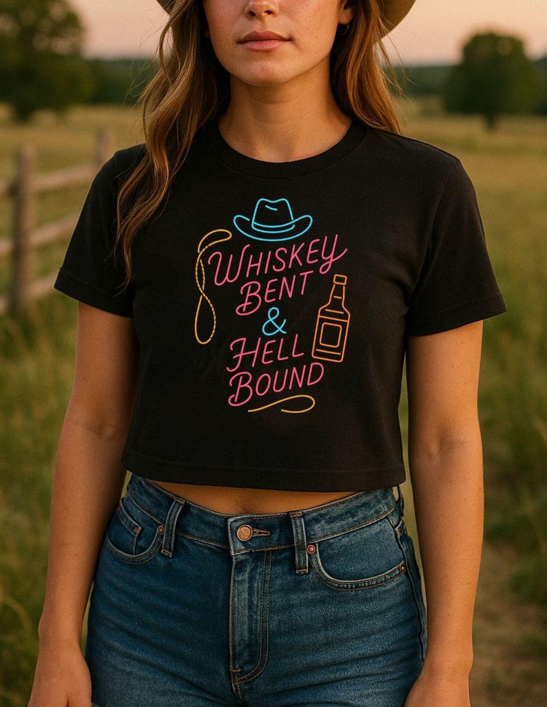 Puede incluir: Top corto negro con el texto de ne&oacute;n "Whiskey Bent & Hell Bound" con un sombrero de vaquero y un gr&aacute;fico de botella de whisky. La camiseta se combina con vaqueros azules. El dise&ntilde;o es en rosa, amarillo y azul.
