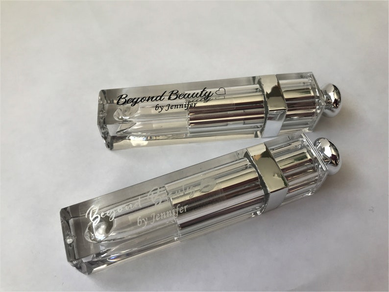 May include: Two clear, rectangular cosmetic containers with silver accents and a rounded silver cap. The text "Beyond Beauty by Jennifer" is printed on the side of each container. The containers are on a white surface.