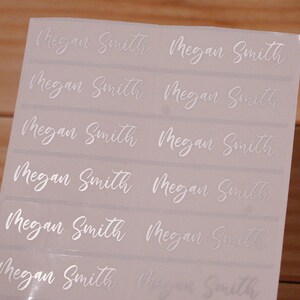 May include: A sheet of rectangular stickers with the name "Megan Smith" printed in a cursive font. The text is in a silver color, and the stickers are arranged in rows and columns.