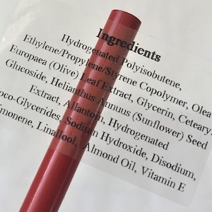 May include: Close-up of a red lip liner pencil with a label displaying the ingredients. The label includes ingredients such as Hydrogenated Polyisobutene, Olea Europaea (Olive) Leaf Extract, and Vitamin E.