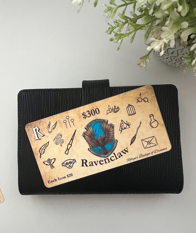 May include: A brown and tan card with a blue and gold Ravenclaw crest and the text "$300 Ravenclaw Robyn's Budget of Dreams Each Icon $20". The card is on a black planner.