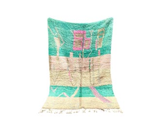 May include: A turquoise and cream Moroccan rug with a geometric pattern. The rug has a fringe border and is made of wool.