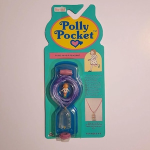 May include: A vintage Polly Pocket "Pixie in Her Pendant" toy, in its original packaging. The teal and pink packaging features the Polly Pocket logo, a small doll, and a pendant necklace. The pendant contains a miniature doll.