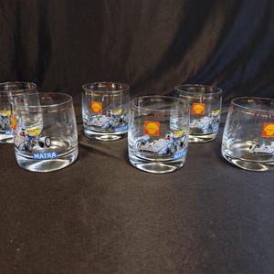 May include: Six clear glass tumblers with a gold rim and a printed image of a blue and white race car with the words "Shell" and "Matra" on them.
