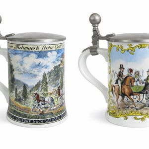 May include: Two white ceramic beer steins with detailed historical scenes. Each stein has a metal lid and handle. One depicts a landscape with a horse-drawn carriage, the other shows people riding horses and a carriage. The steins have text at the top and bottom.
