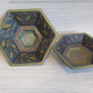 Könnte beinhalten: Zwei sechseckige Keramikschalen. Die größere Schale ist blau mit Blatt- und geometrischen Mustern, die kleinere Schale hat ein ähnliches Design. Die Schalen haben einen zentralen Sechseck mit einem floralen Design.