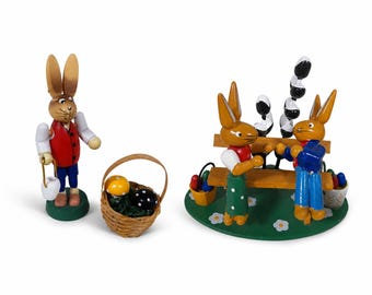 Peut inclure: Figurines de lapin de Pâques en bois. Un lapin tient un seau, un autre est avec un panier d'œufs. Deux lapins sont assis sur un banc avec des œufs décoratifs. Les figurines sont peintes avec des couleurs vives et sont sur une base verte.