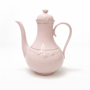 Puede incluir: Una tetera de cerámica rosa con un pico y asa curvados. La tetera tiene una tapa con un adorno floral y ribete dorado. Un patrón floral decorativo está en relieve en el cuerpo de la tetera.