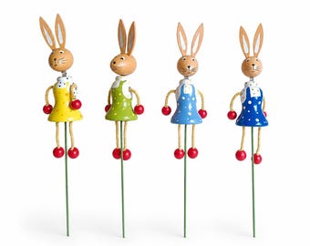 Peut inclure: Quatre figurines de lapin en bois avec des détails peints. Chaque lapin porte une robe de couleur différente avec des pois blancs. Les lapins sont sur des bâtons et sont disposés en rangée.