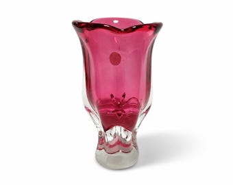 Può includere: Un vaso in vetro color magenta vivace con una base in vetro trasparente e un bordo ampio e ondulato. L'interno del recipiente è di un rosa profondo e saturo, mentre la base esterna rimane trasparente, creando un netto contrasto cromatico.