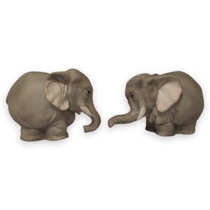Puede incluir: Dos figuras de elefantes grises con detalles precisos, incluyendo grandes orejas y trompas curvadas. Los elefantes se enfrentan, creando una sensación de interacción. Las figuras están hechas de un material sólido y tienen un acabado liso. El fondo es blanco.