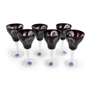 Könnte beinhalten: Ein Set aus sechs Weingläsern mit tiefroten Kelchen, die komplexe Schliffmuster wie Kreismotive und Sternformen aufweisen. Jedes Glas hat einen klaren, facettierten Stiel und einen runden Fuß, wobei an jedem ein kleiner blauer Aufkleber haftet.