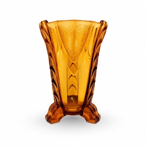 Può includere: Vaso in vetro color ambra con design Art Déco. Il vaso ha una superficie strutturata, una parte superiore svasata e una base a tre piedi. Un oggetto decorativo.