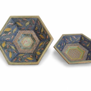 Può includere: Due ciotole esagonali in ceramica con interno blu decorato da motivi a foglie gialle e rosa. Il centro di ogni ciotola presenta un design geometrico a reticolo in tonalità tenui, con un piccolo motivo centrale nella ciotola più grande.