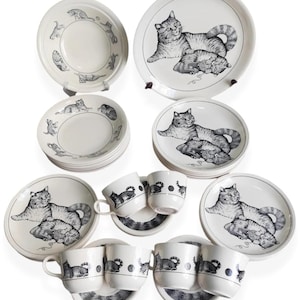 Può includere: Una collezione di stoviglie in ceramica bianca con illustrazioni di gatti in bianco e nero. Il set comprende piatti, ciotole, tazze e piattini. I disegni dei gatti variano.