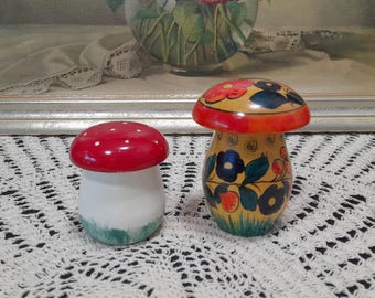 May include: Two wooden mushroom shaped salt and pepper shakers. The larger shaker is painted with yellow, green, red, and black floral designs. The smaller shaker is painted red with white polka dots and has a white base with green accents.