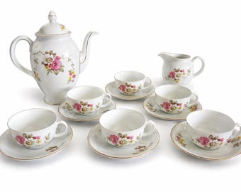 May include: A white porcelain tea set featuring a teapot, creamer, and six teacups with saucers. Each piece is adorned with a floral pattern in pink, yellow, and brown, with gold trim. A classic tea party set.