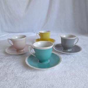 May include: Set of four colourful teacups and saucers. The cups are white with a coloured band around the top. The colours are pink, yellow, grey, and turquoise.