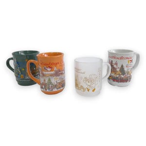 May include: Four ceramic mugs featuring holiday designs. One dark green mug, one orange mug with Nürnberger Christkindlesmarkt text, one frosted white mug with gold graphics, and one white mug with a colorful market scene and 175 text.